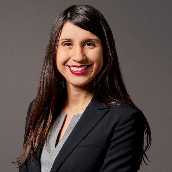 Smiling woman in a business suit with long dark hair against a gray background.