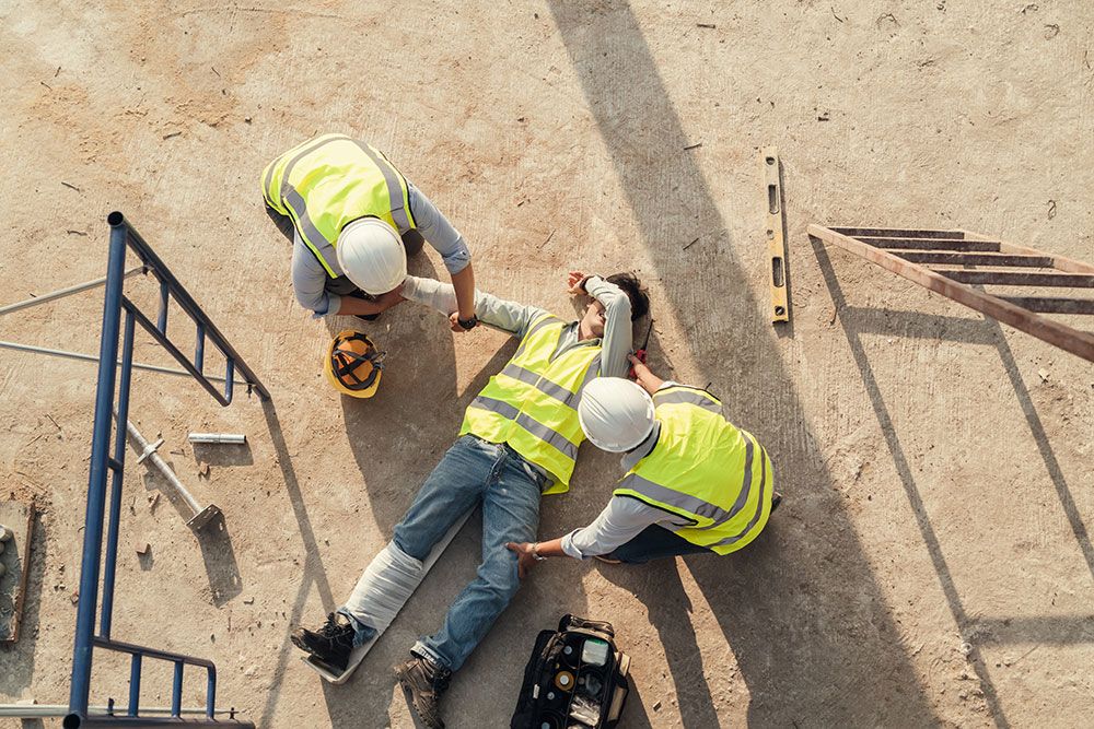 Construction site accident, workers in safety gear helping injured colleague on the ground.