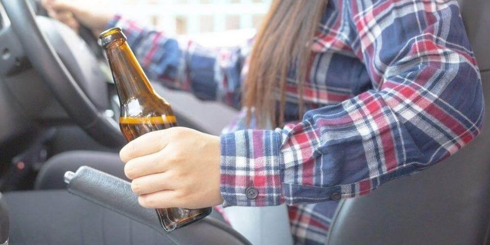 Woman driving a car with an open beer, illustrating