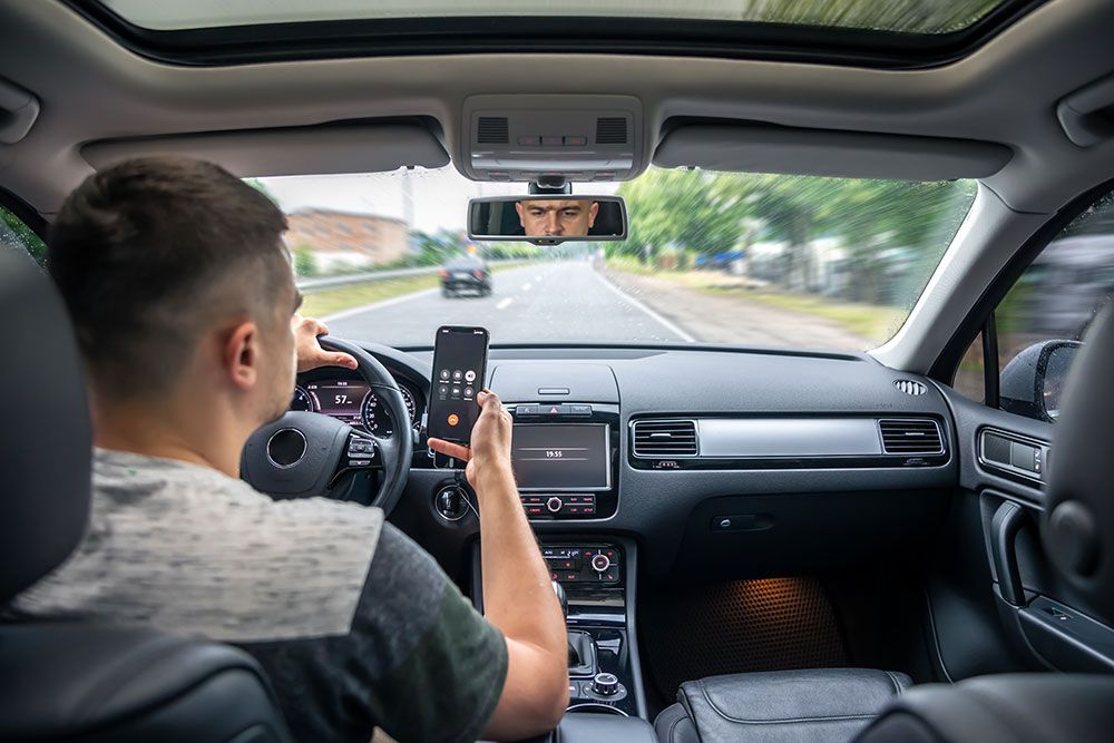 Driver using smartphone while driving car, focusing on device instead of road. Potential distracted driving risk.