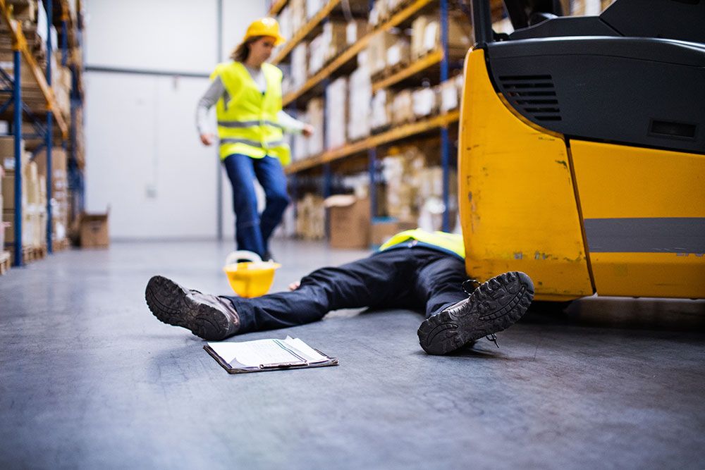 Warehouse accident scene with worker injured by forklift, safety helmet and clipboard nearby in industrial setting.