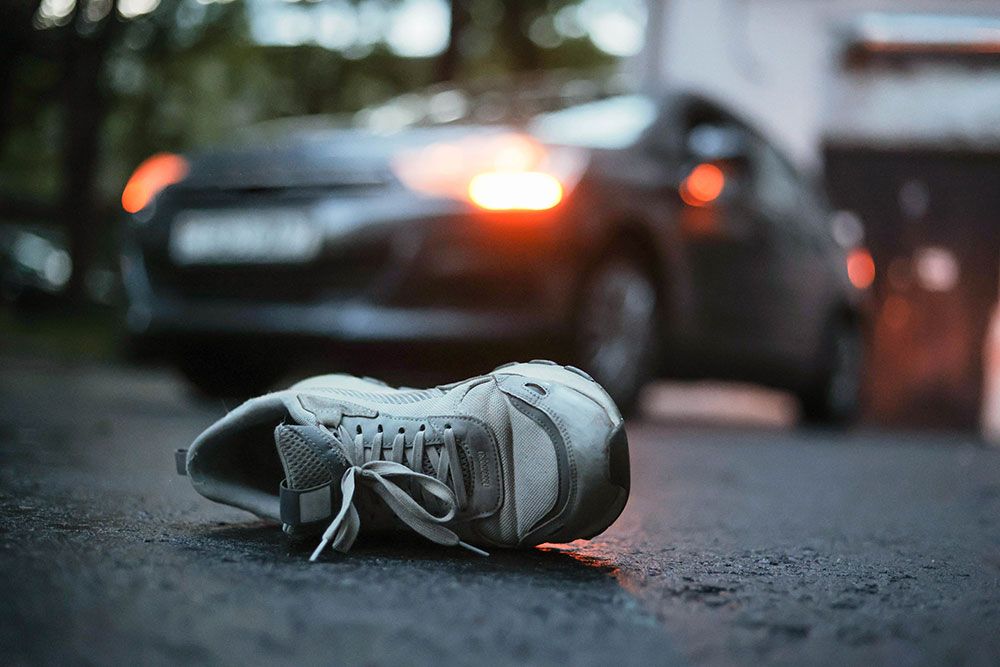 Single white sneaker on road in front of car with headlights on, suggesting an accident scene.