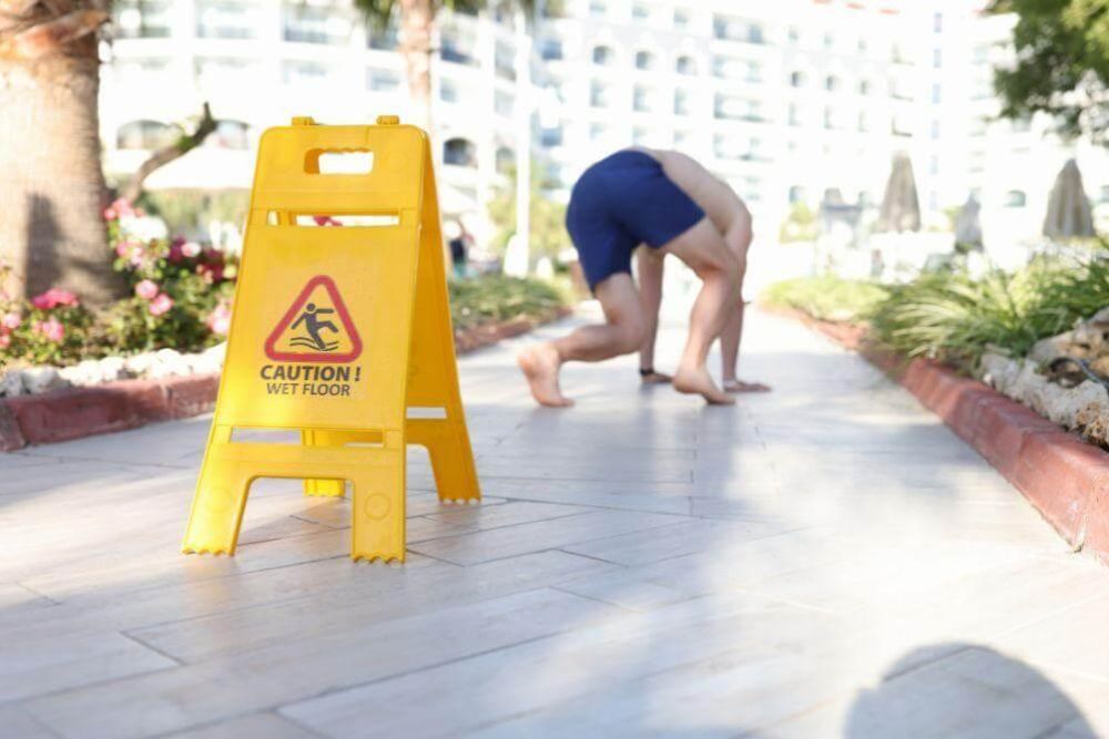 A person bending over near a caution wet floor sign