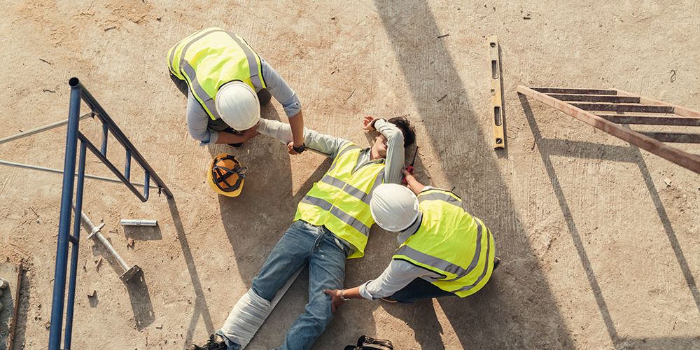 Construction site accident, workers in safety gear helping injured colleague on the ground.