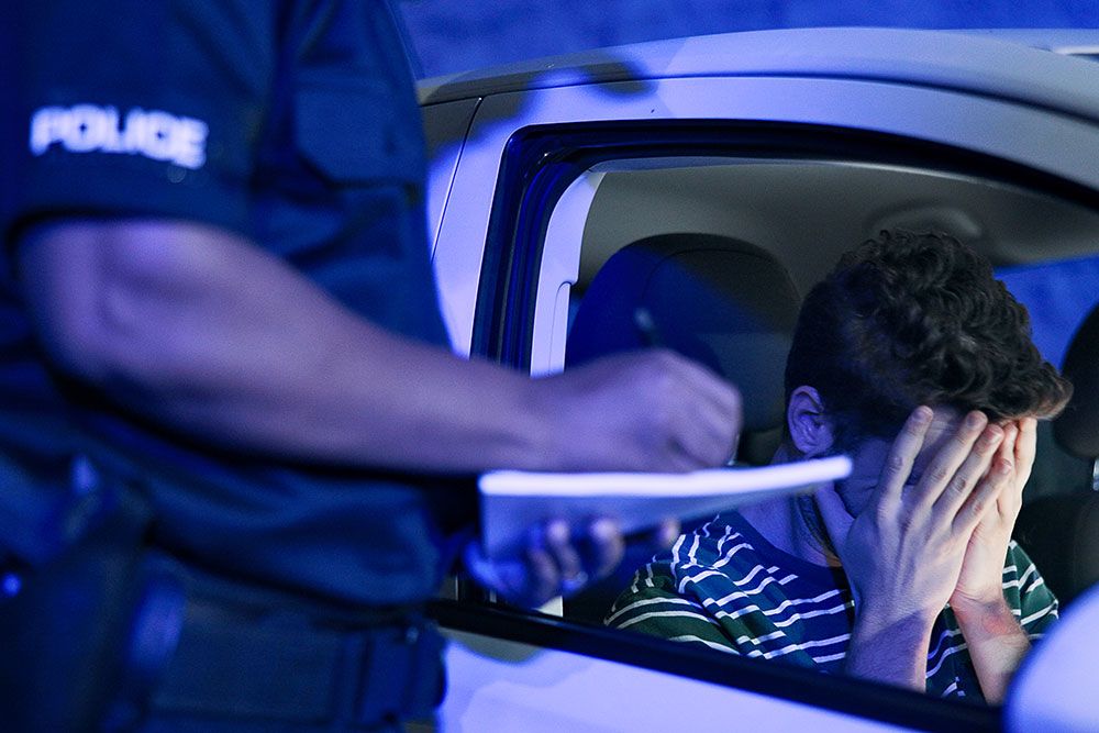 Police officer issuing ticket to distressed driver in parked car at night.