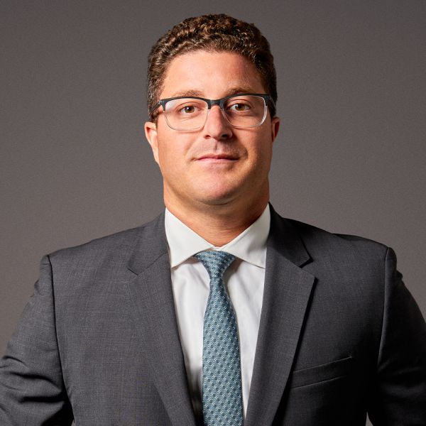 Professional man in a suit and glasses, standing confidently against a gray background.