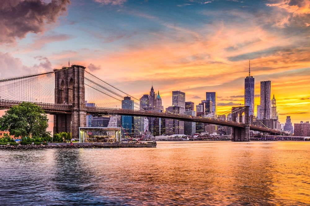 Sunset view of the Brooklyn Bridge with New York City skyline in the background and vibrant sky.