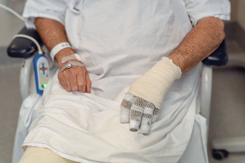 Patient in hospital gown with bandaged hand in wheelchair, close-up view.