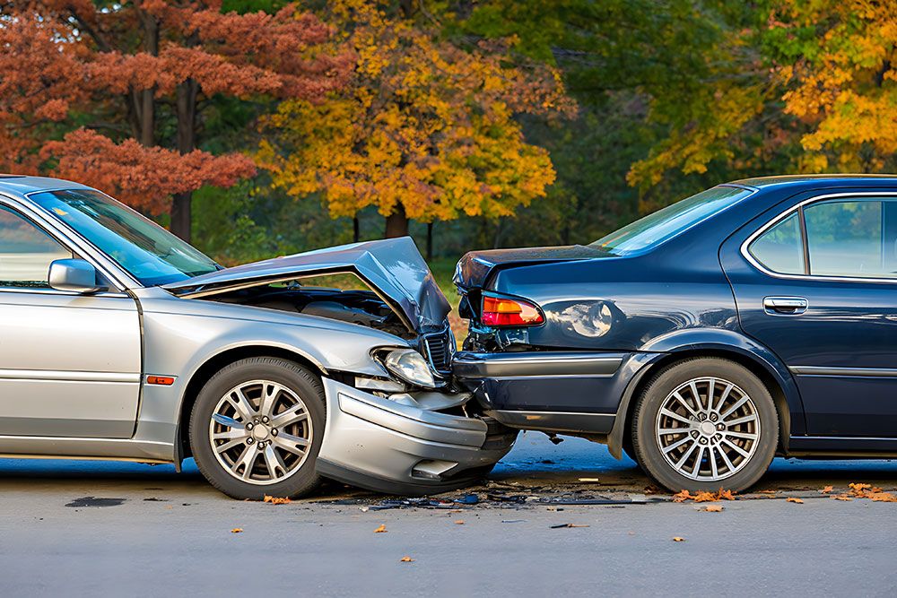 Two cars in a rear-end collision with autumn trees in the background, showing vehicle damage.