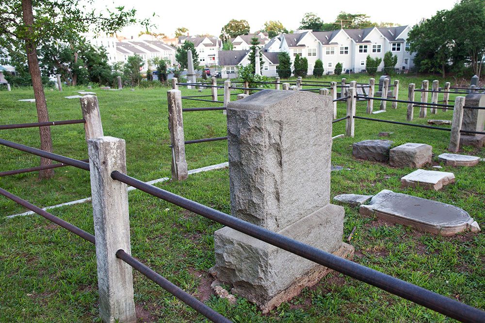 Historic cemetery with weathered gravestones and fencing near residential area.