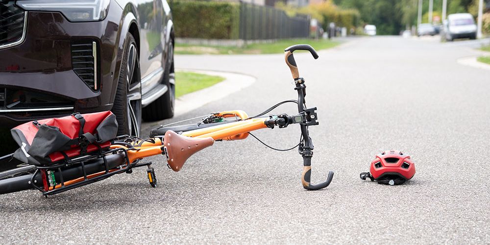 Orange bicycle and red helmet on road beside a parked car, suggesting an accident or collision scene.