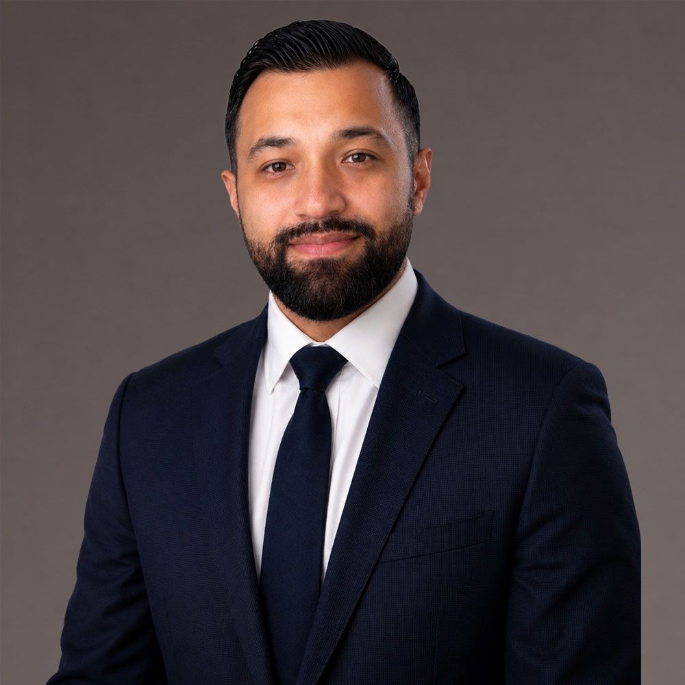 Fernando Ramos in navy suit and tie smiling, against a gray background. Ideal for business profiles or corporate use.