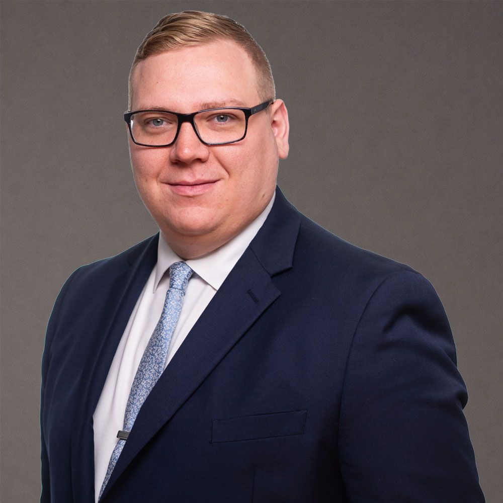 Robert Baurley in a suit and tie with glasses, posing against a gray background.