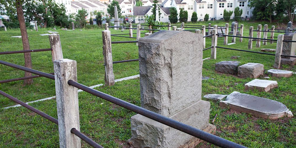 Historic cemetery with weathered gravestones and fencing near residential area.
