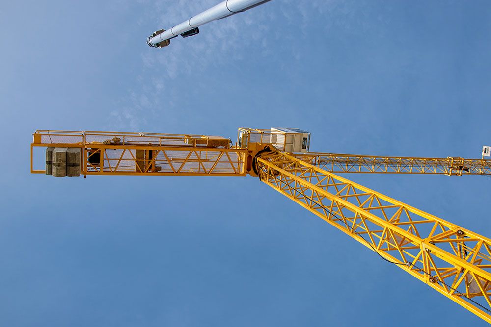 Yellow construction crane against clear blue sky, viewed from below.