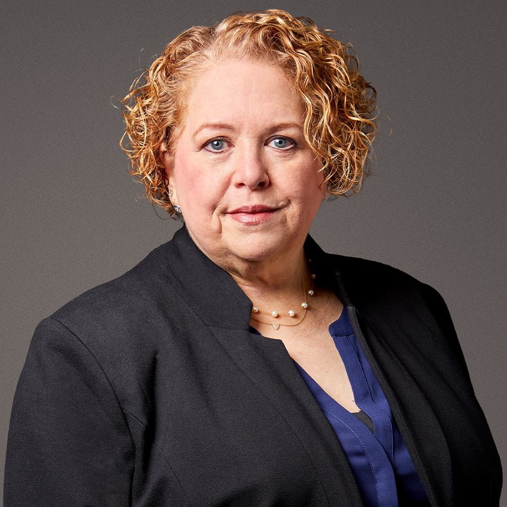 I don’t know who this is, but here's an alt text you can use: Professional woman with curly hair in business attire, neutral background.