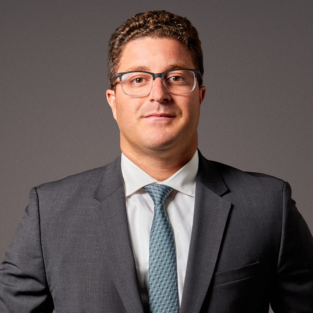 Professional man in a suit and glasses, standing confidently against a gray background.