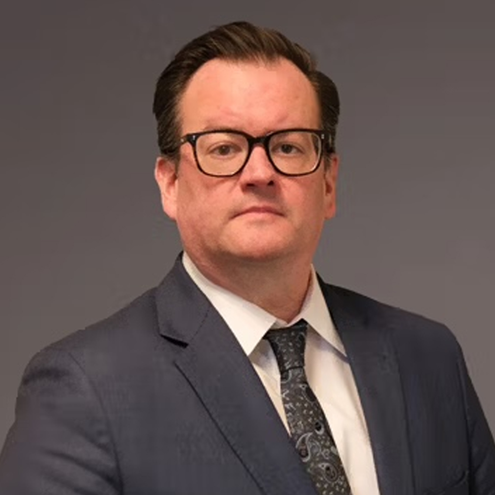attorney chad russell in a suit and tie with glasses looks confidently at the camera against a gray background.