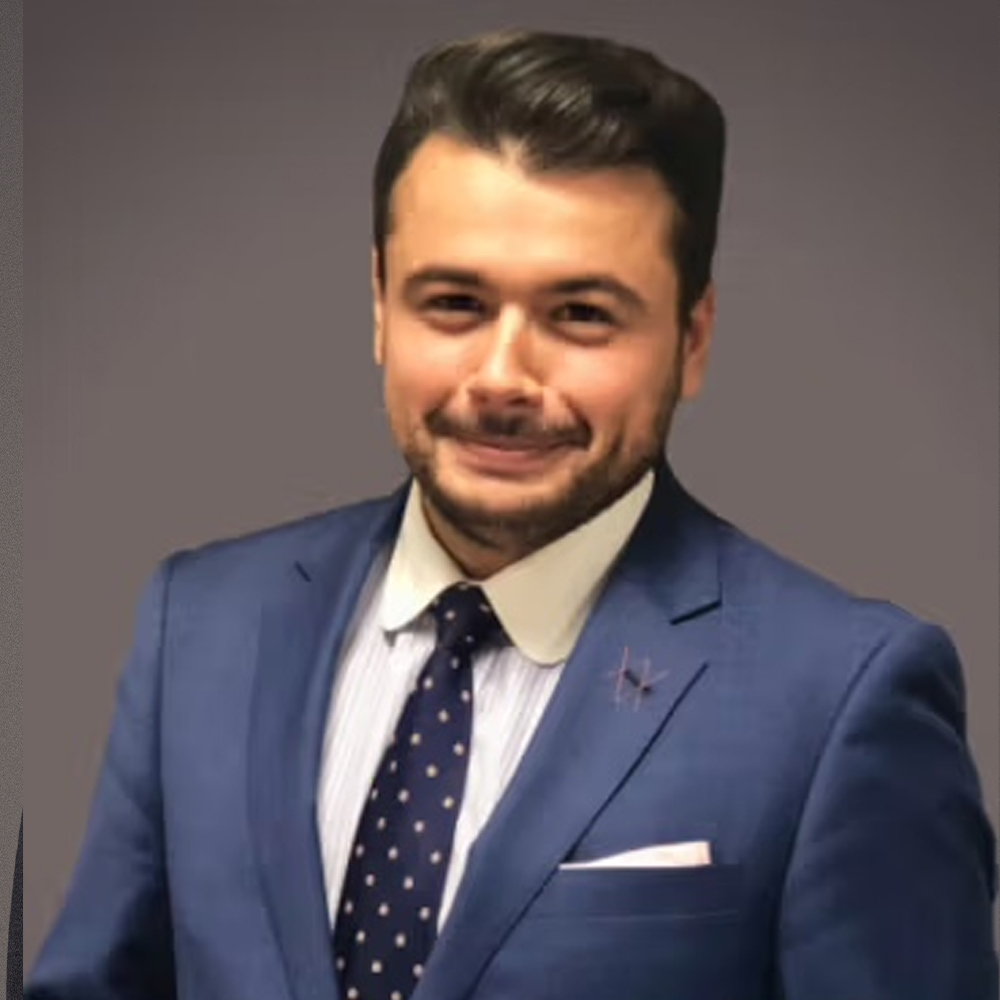 Professional man in a blue suit and polka dot tie smiling against a gray background.