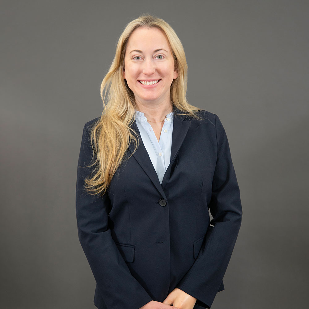 Carly Janetty in a navy blazer and light blue blouse on a gray background, showcasing a professional appearance.